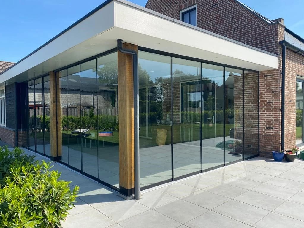 Sliding glass walls around a covered terrace beside a brick house